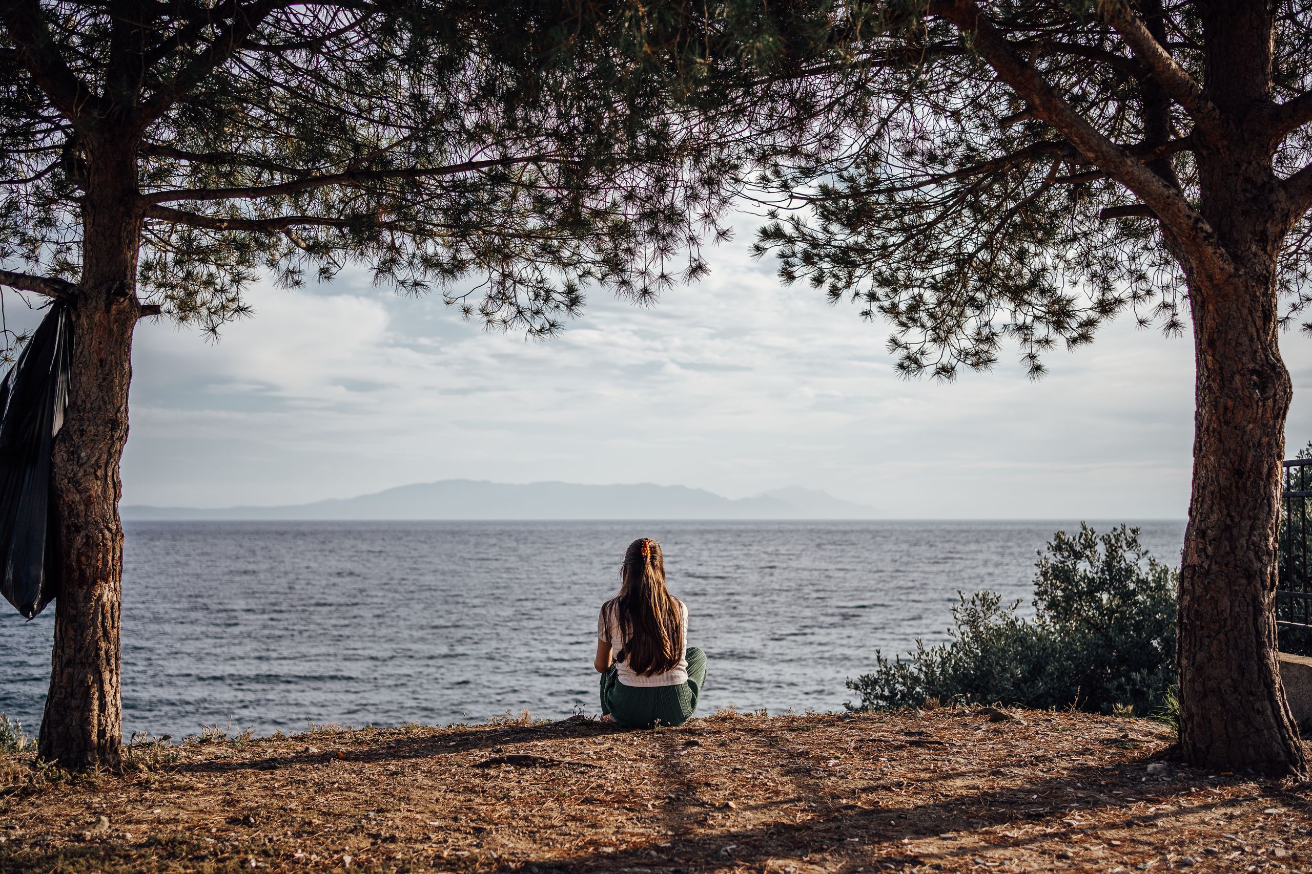 A woman practicing being in the present by the sea in Ozdere, Turkey, with a scenic view of nature and water.